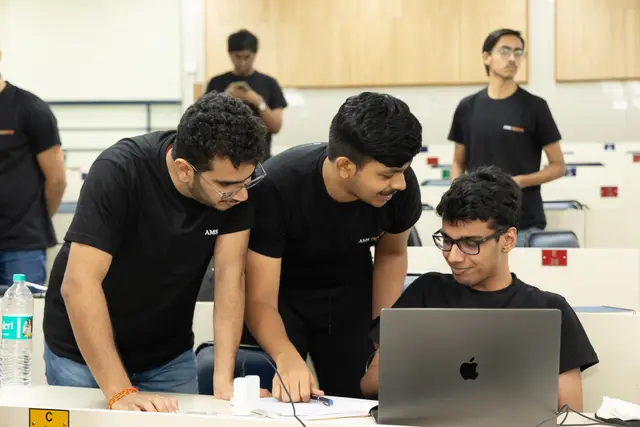 Three students huddled over a laptop and notes in the contest hall, talking through a solution